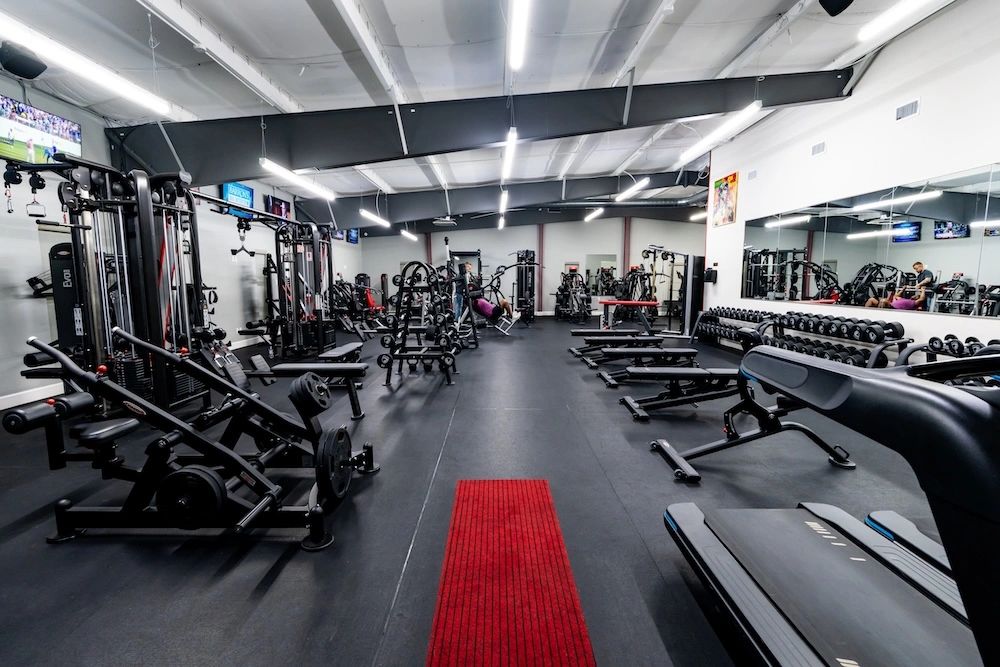WEF strength floor wide establishing &mdash; machines, dumbbell rack, mirror wall, the long red line