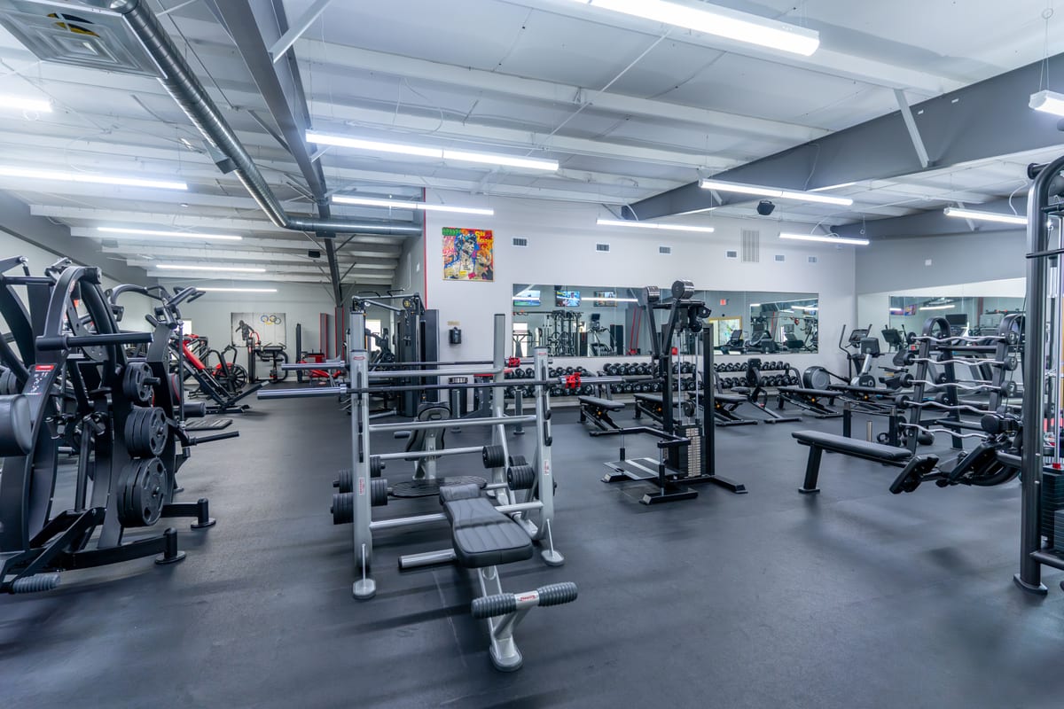 Olympic bench-press stations and the mirrored dumbbell wall on the strength floor